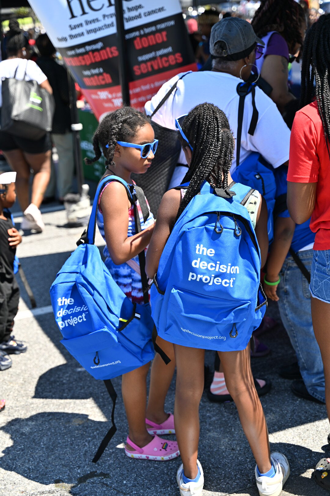 Our History Two children are standing together at an Infinite Legacy Block Party with Decision Project backpacks.