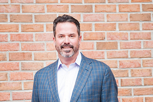 President and Chief Executive Officer, Charlie Alexander stands in front of Infinite Legacy's office, wearing a suit.